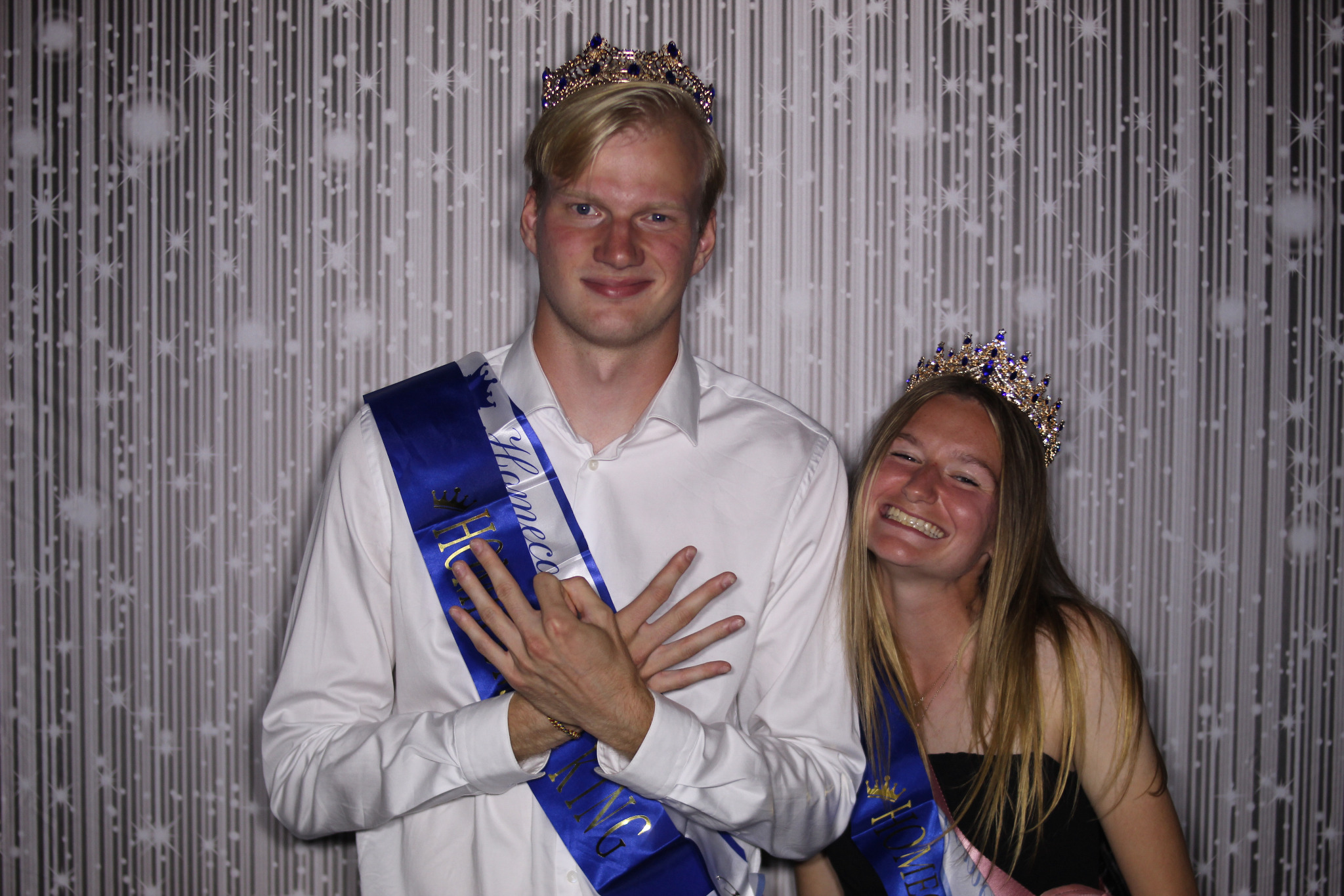 College homecoming king and queen smiling together in the Lotsa Laffs photo booth, comfortably framed despite a large difference in height.